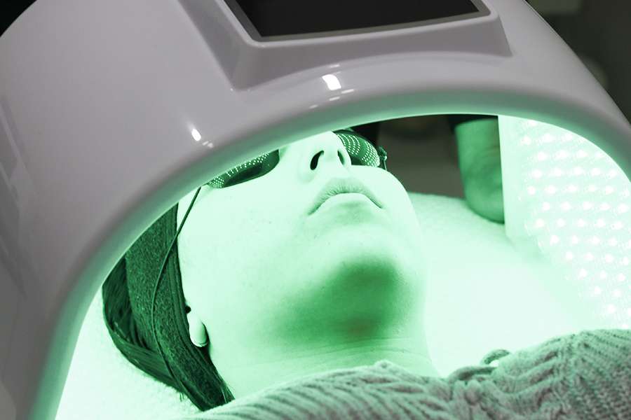 LED-light-therapy Woman's face laying beneath green LED light therapy machine.