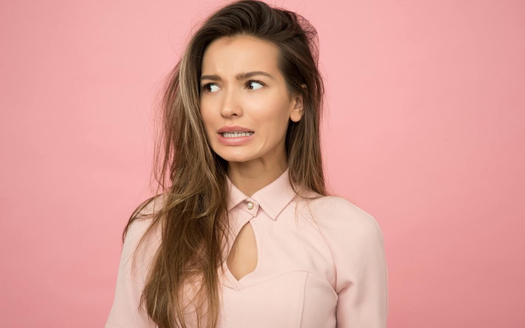 A woman standing in front of a pink background looking confused at considering a visit to a Winnipeg Skin Clinic to learn about skin repair from daylight exposure