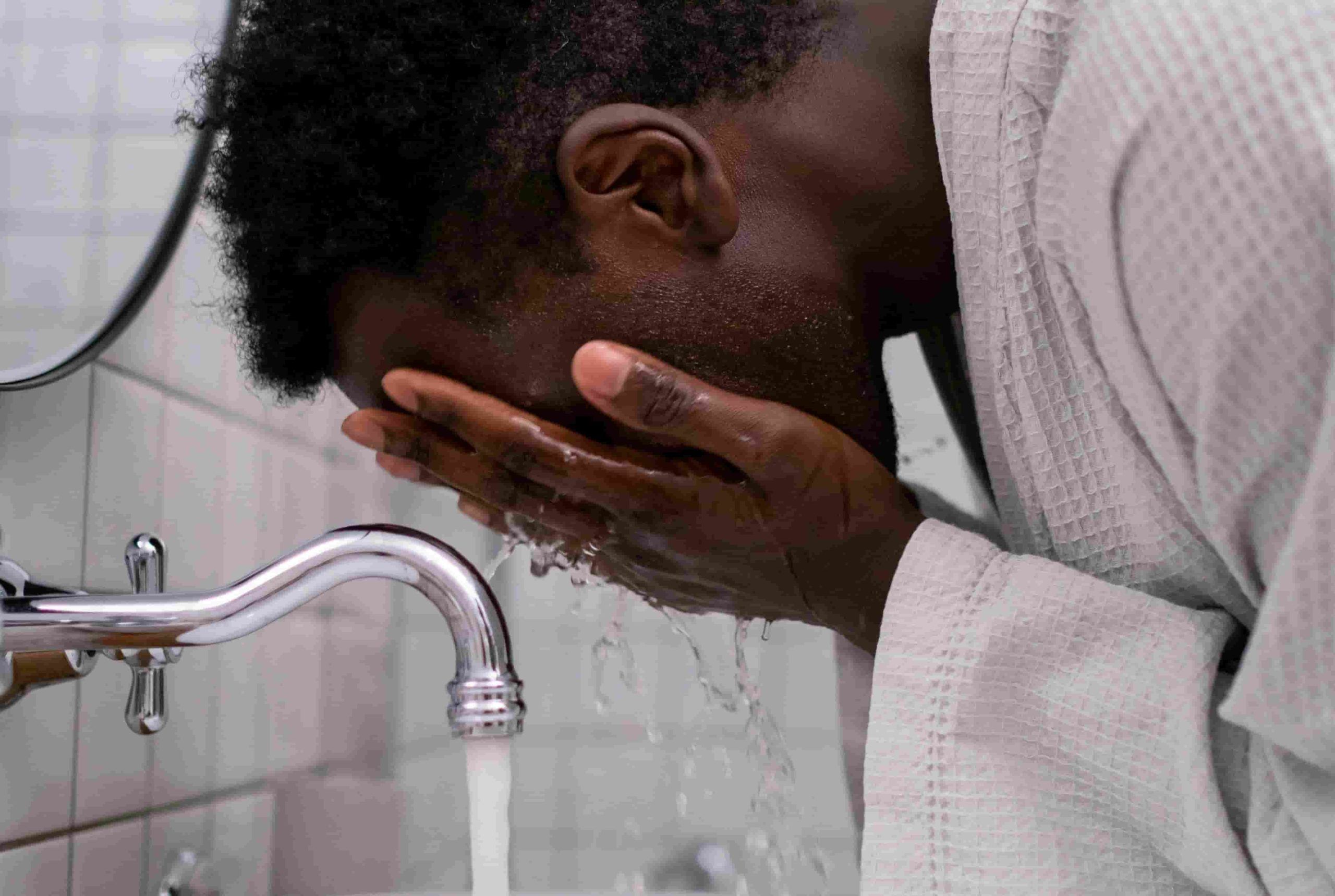Man washing his face with water, a reminder that Skincare Tips for Travelling include cleansing to fight dryness and breakouts after long flights.