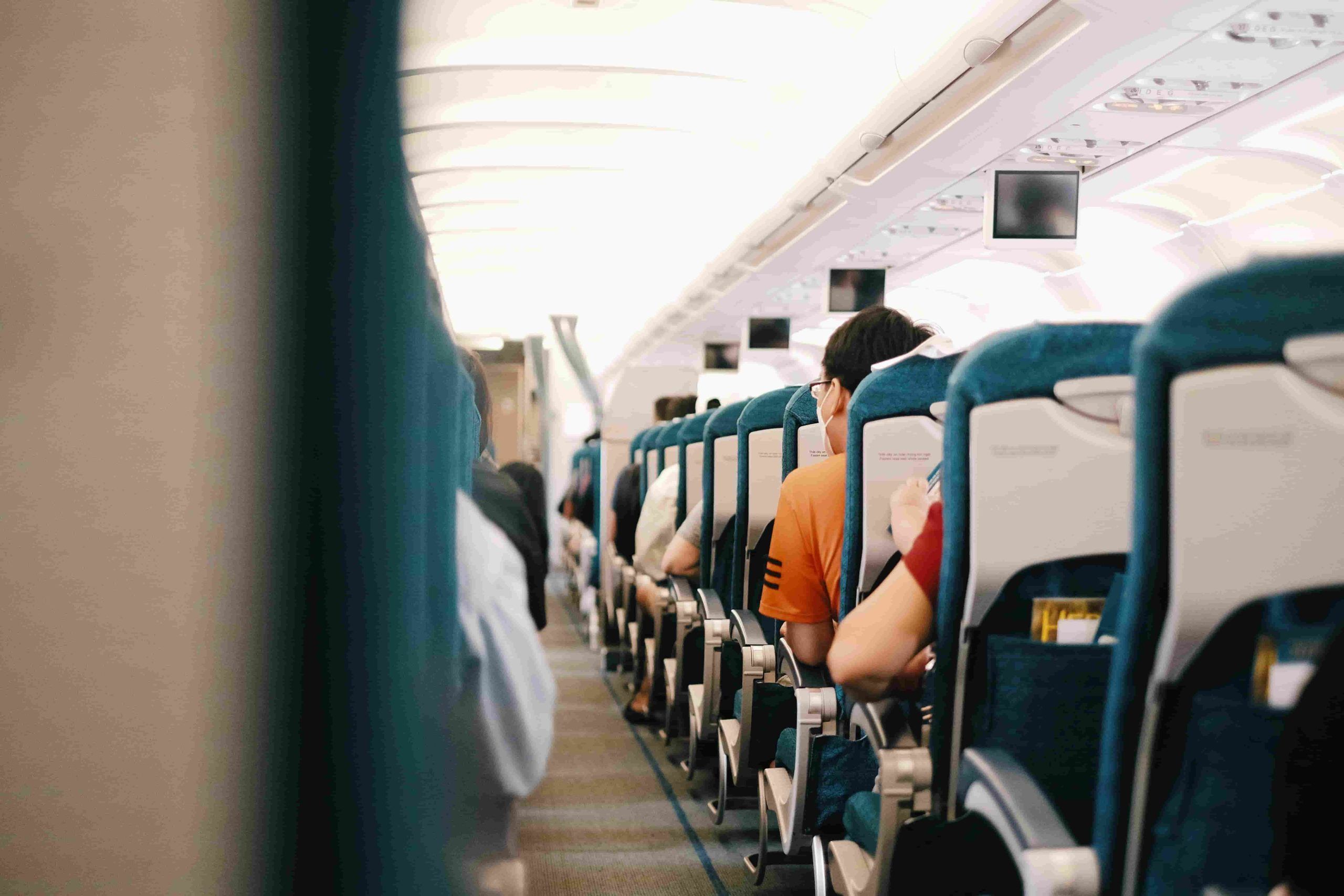 Airplane cabin with passengers seated during a long-haul flight, illustrating the need for Skincare Tips for Travelling to stay hydrated and refreshed.