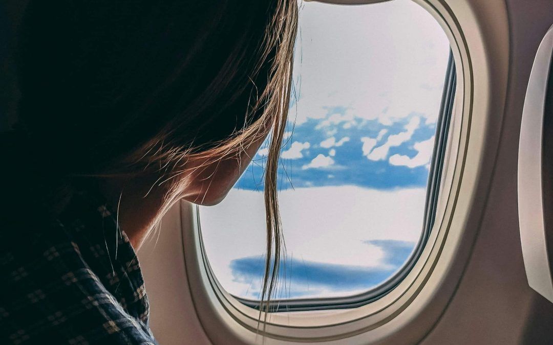 Woman looking out an airplane window, highlighting Skincare Tips for Travelling such as hydration and protecting skin from dry cabin air.