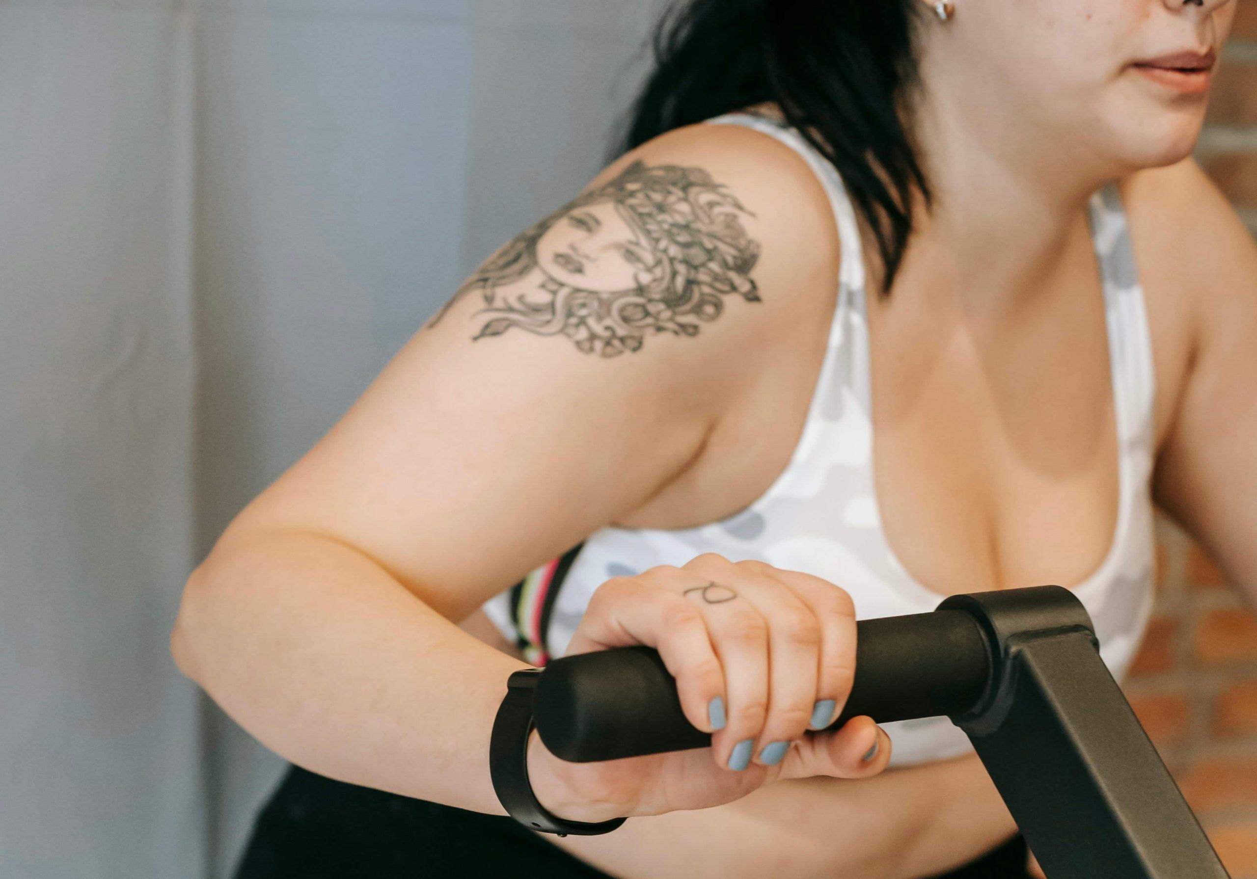 Woman exercising on a stationary bike, wearing a sports bra and showcasing a floral tattoo on her upper arm.